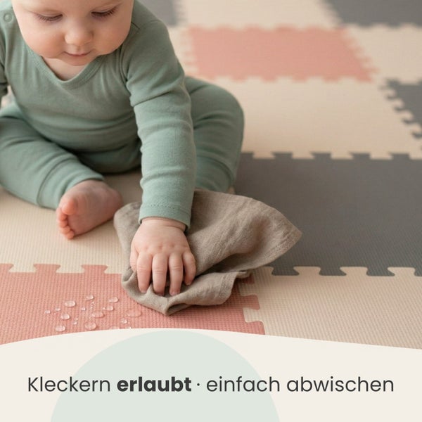 Ein Baby sitzt auf einer Puzzlematte aus Schaumstoff und wischt verschüttete Flüssigkeit mit einem Tuch ab.