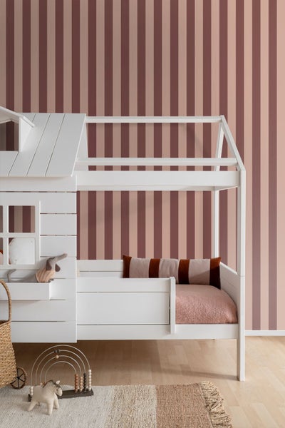 Weißes Hausbett aus Holz in einem hellen Kinderzimmer vor einer gestreiften Tapete.