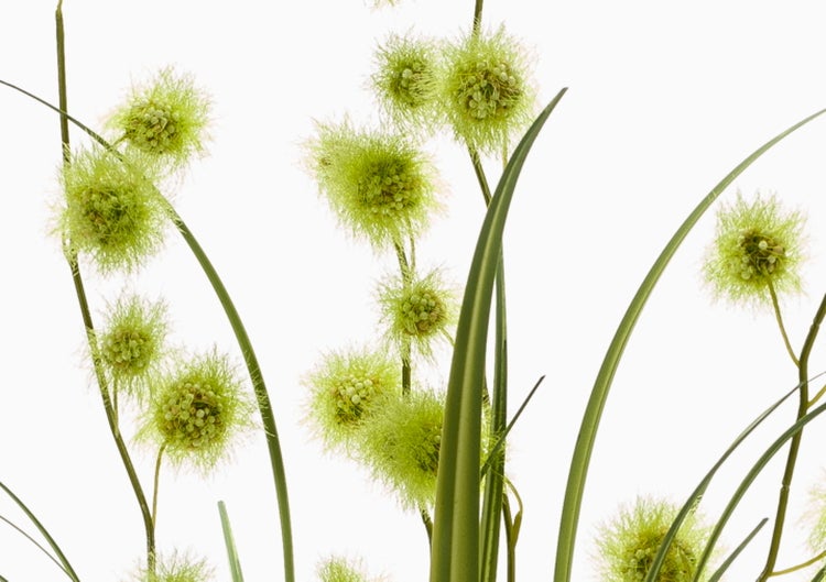 Künstliche Pflanze mit langen grünen Blättern in einem schwarzen Blumentopf aus Kunststoff.