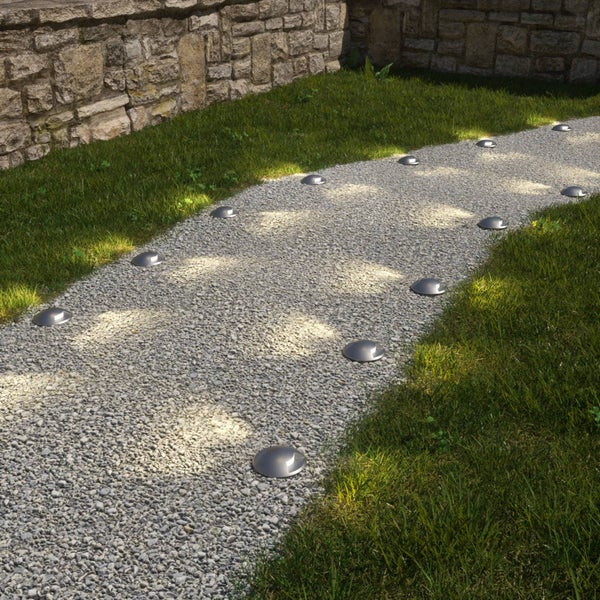 Solar-Bodenleuchten auf einem Kiesweg im Garten entlang einer Natursteinmauer.