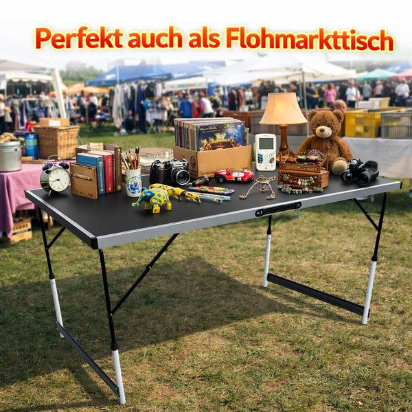 Klappbarer Campingtisch auf einer Wiese, genutzt als Flohmarktstand mit verschiedenen Gegenständen wie Spielzeug und Büchern darauf.