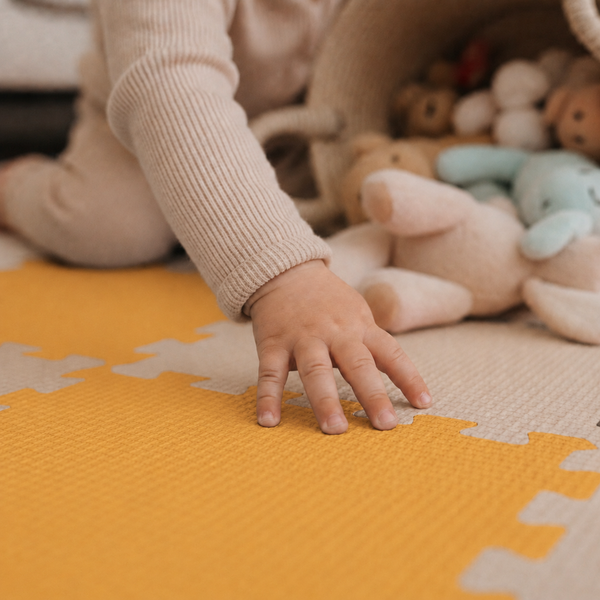 Kind spielt auf einer Puzzlematte aus Schaumstoff mit Kuscheltieren in einem Korb.