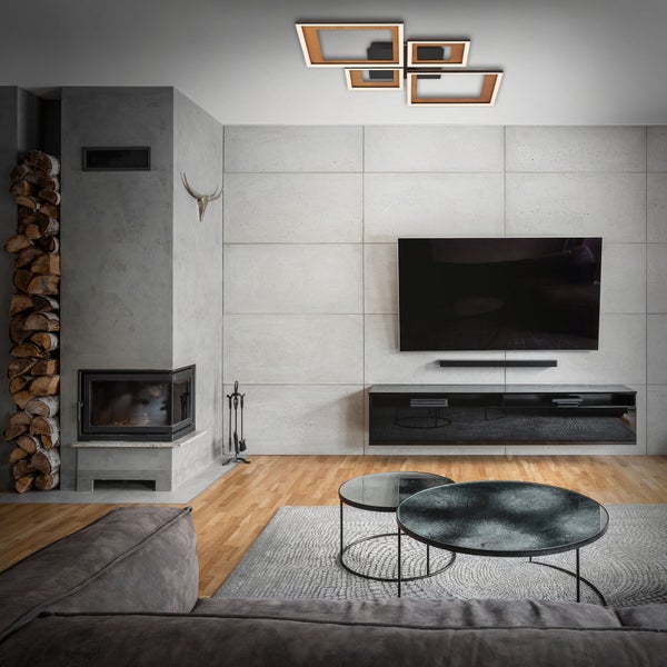 Modernes Wohnzimmer mit geometrischer LED Deckenleuchte, Wand in Betonoptik mit Fernseher, Kamin mit Kaminholz und hellem Holzboden.
