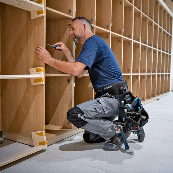Handwerker auf Leiter mit Werkzeugtasche bei Installationsarbeiten in Küche
