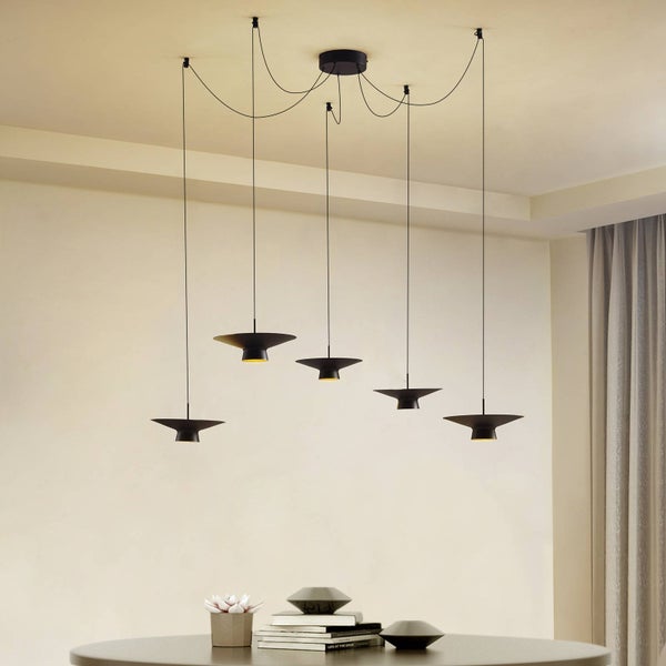 Moderne fünfflammige Pendelleuchte in Schwarz mit flachen Metallschirmen, höhenversetzt über einem Tisch in einem hellen, organisierten Raum.
