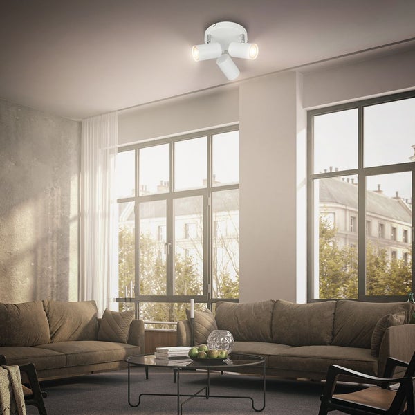 Dreiflammiger weißer Deckenstrahler in einem modernen, hellen Wohnzimmer mit großen Fenstern und braunen Sofas.