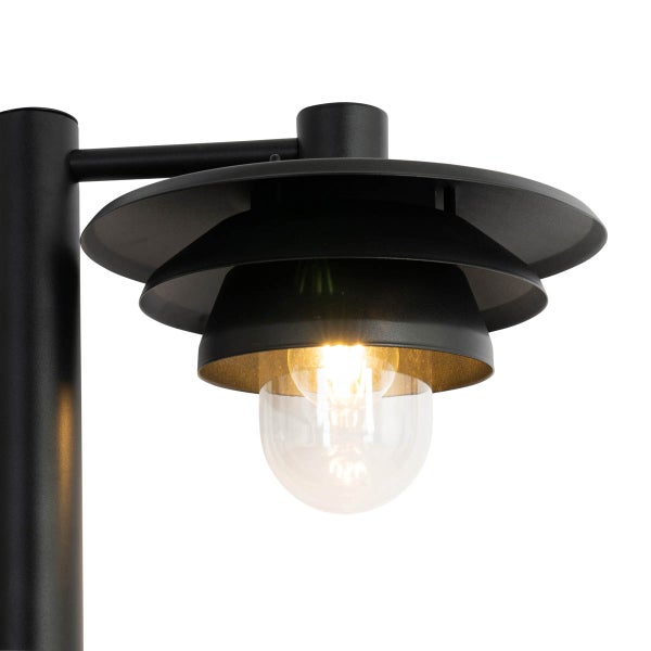 Detailansicht einer schwarzen Außenleuchte mit mehrstufigem Schirm und leuchtendem Leuchtmittel hinter Klarglas.