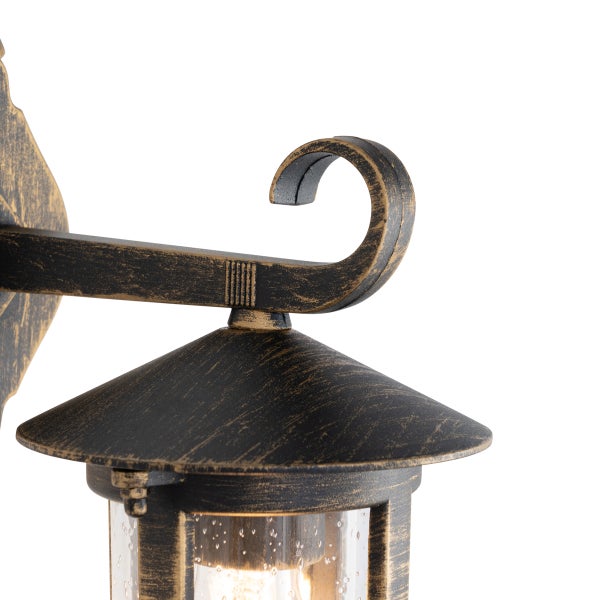 Außenwandleuchte aus schwarz-goldfarbenem Metall im antiken Stil mit geschwungenem Arm und Glaseinsatz.