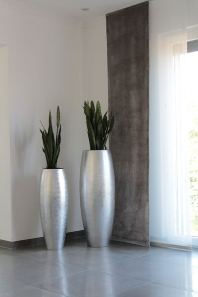 Zwei hohe, silberne Bodenvasen mit Bogenhanf in einem hellen, minimalistischen Raum.