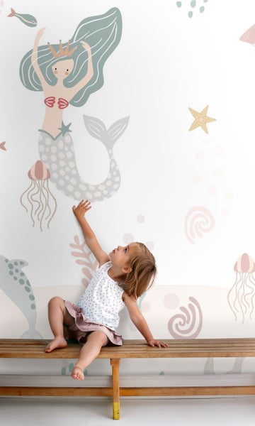 Mädchen sitzt auf Bank vor Wandtattoo mit Meerjungfrau, Delfin und Quallen