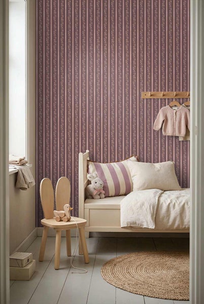 Gestreifte Vliestapete mit floralem Muster in einem hellen Kinderzimmer mit Holzbett, Stuhl mit Hasenohren und rundem Juteteppich.