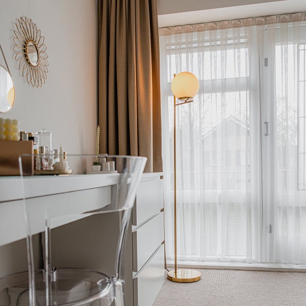 Zimmer mit Schminktisch, transparentem Stuhl, Stehlampe und Vorhängen