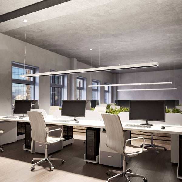 Moderne Bürobeleuchtung mit langen weißen LED-Pendelleuchten über Arbeitsplätzen in einem hellen Büro mit Sichtbeton-Decke.