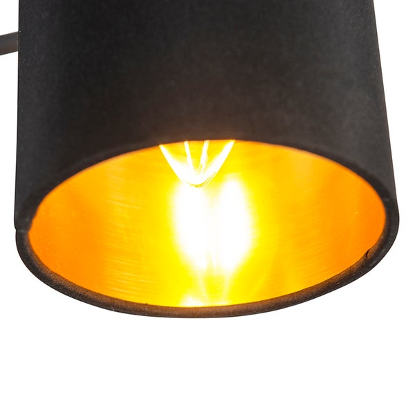 Nahaufnahme eines Lampenschirms aus Stoff mit goldfarbener Innenseite und leuchtendem Leuchtmittel.