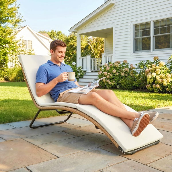 Ein Mann entspannt auf einer ergonomisch geformten Gartenliege mit weißer Auflage auf einer gepflasterten Terrasse im Garten.