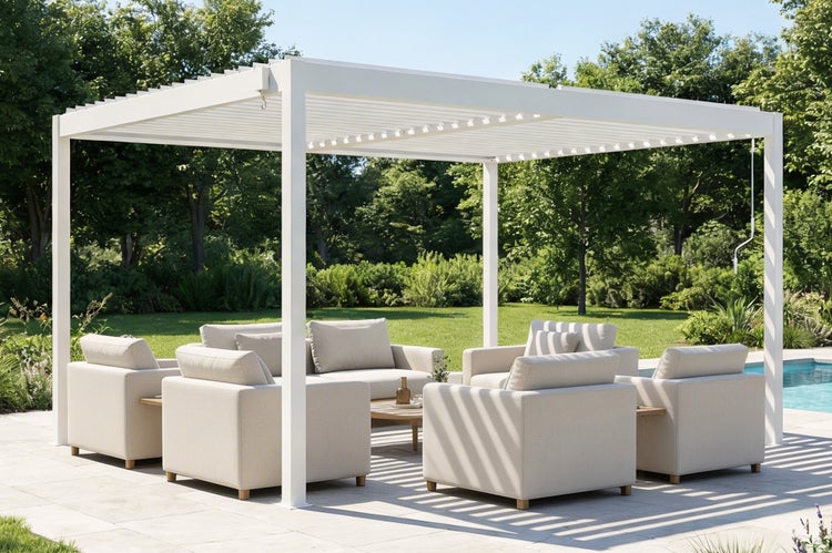 Freistehende weiße Lamellenpergola über einem modernen Lounge-Set mit Sesseln und Sofa auf einer gepflasterten Terrasse neben einem Garten.