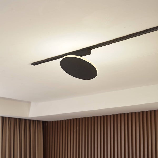 Schwarzer, runder Strahler für ein Stromschienensystem an der Decke mit indirektem Lichteffekt.