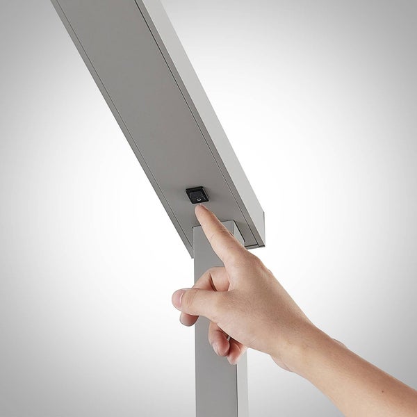 Hand betätigt den Wippschalter an einer grauen Metallleuchte.