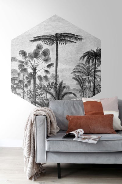 Wohnszene mit einer sechseckigen Tapete mit Palmenmotiv über einem grauen Sofa mit Kissen und Decke.