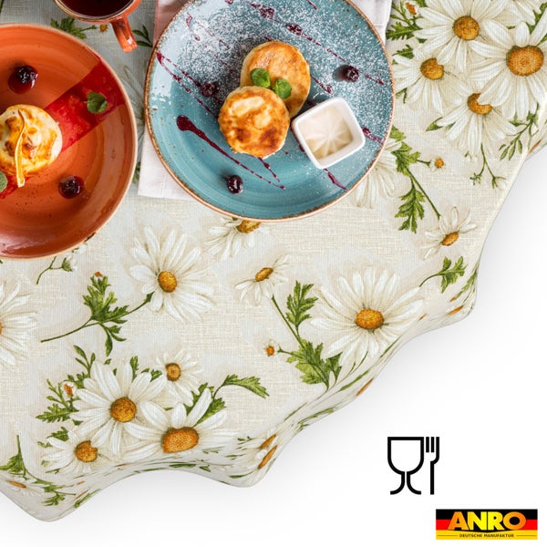Tischdecke mit Gänseblümchen-Muster und Textilstruktur, gedeckt mit Tellern und Speisen in heller Atmosphäre. Lebensmittelecht. ANRO Deutsche Manufaktur Logo.