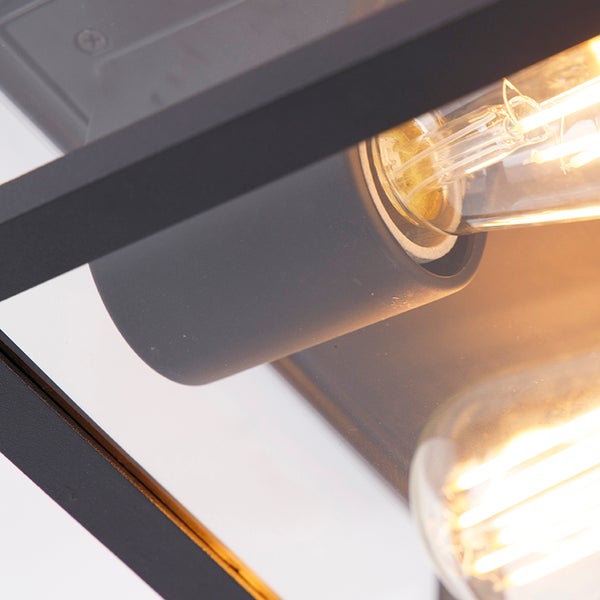 Nahaufnahme einer Wandleuchte mit E27-Fassung und LED-Filament-Leuchtmittel in einem schwarzen Metallrahmen.