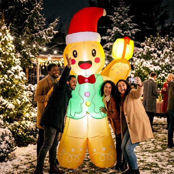 Eine Gruppe von Menschen macht ein Selfie mit einer großen, leuchtenden, aufblasbaren Lebkuchenmann-Dekoration in einer winterlichen Gartenkulisse.