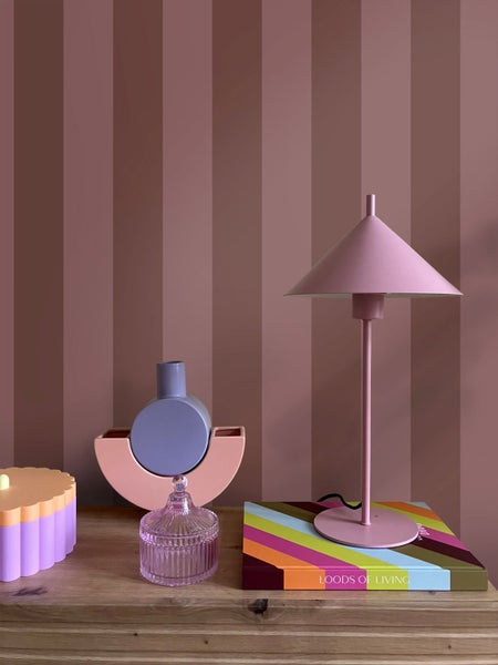 Gestreifte Tapete in Mauve-Tönen hinter einem Sideboard mit einer Tischlampe, Vasen und Wohnaccessoires in modernem Design.