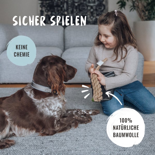 Mädchen spielt mit Hund und Baumwollspielzeug im Wohnzimmer. Keine Chemie. 100 Prozent natürliche Baumwolle.