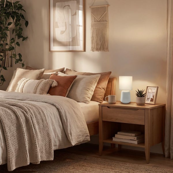 Moderne Tischlampe mit geriffeltem Sockel auf einem Nachttisch in einem gemütlich eingerichteten Schlafzimmer mit Bett und Dekoration.