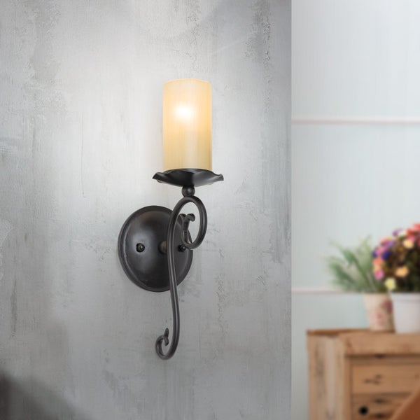 Rustikale Wandleuchte im Fackeldesign mit zylindrischem Glasschirm und geschwungener Metallhalterung an einer Wand montiert.