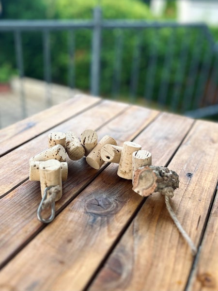 Vogelspielzeug aus Weinkorken und Naturholz mit Metallkarabiner auf einem Holztisch.