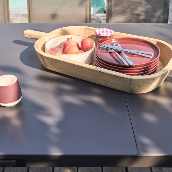 Großes Serviertablett aus Holz auf einem dunklen Gartentisch mit Obstschale, Tellern, Besteck und einem Glas.