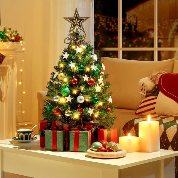 Dekorierter Weihnachtsbaum mit Stern, Kugeln, Lichtern und Geschenken auf einem Tisch.