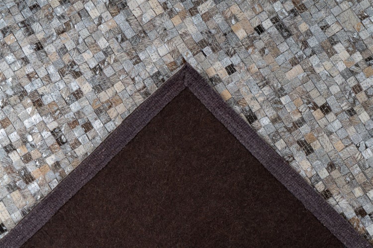 Detailansicht eines Teppichs mit Mosaikmuster aus grauen und beigen Quadraten sowie einer dunkelbraunen Rückseite.