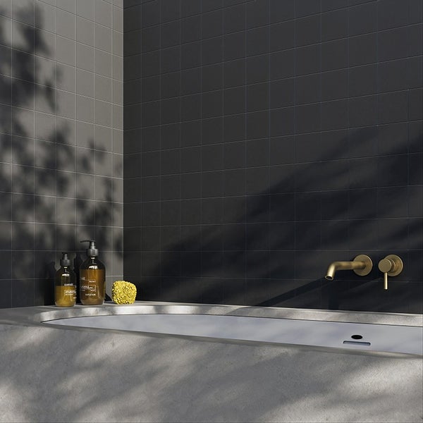 Modernes Badezimmer mit dunklen quadratischen Wandfliesen, einer Badewanne in Betonoptik und einer Unterputz Armatur in Metalloptik.