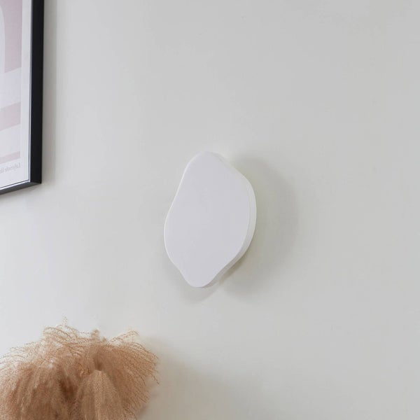 Moderne weiße Wandleuchte in organischer Form in einem hellen Raum mit Trockenpflanzen.