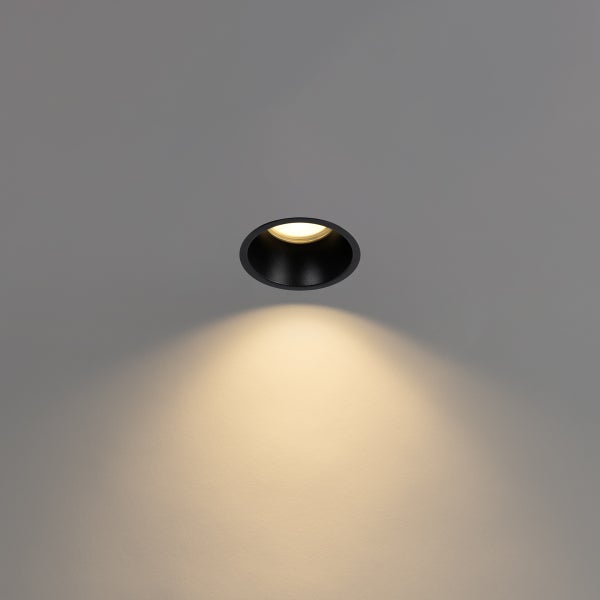 Schwarzer Einbaustrahler an der Decke mit warmweißem Lichtkegel nach unten.