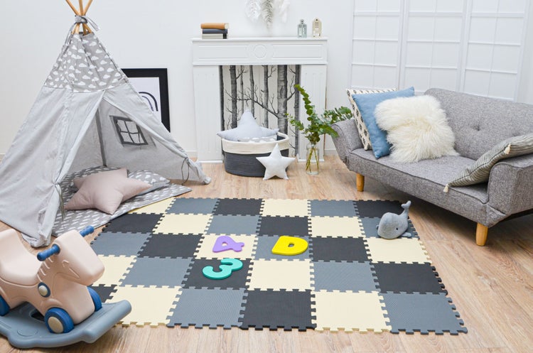 Helles Kinderzimmer mit quadratischer Schaumstoff-Puzzlematte in Grau und Creme, Tipi-Zelt, kleinem Sofa und Spielzeug auf Holzboden.