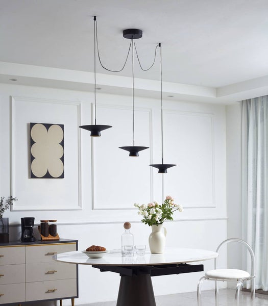 Dreiflammige Pendelleuchte mit schwarzen flachen Schirmen über einem hellen Esstisch mit Marmorplatte in einem modern eingerichteten Raum.