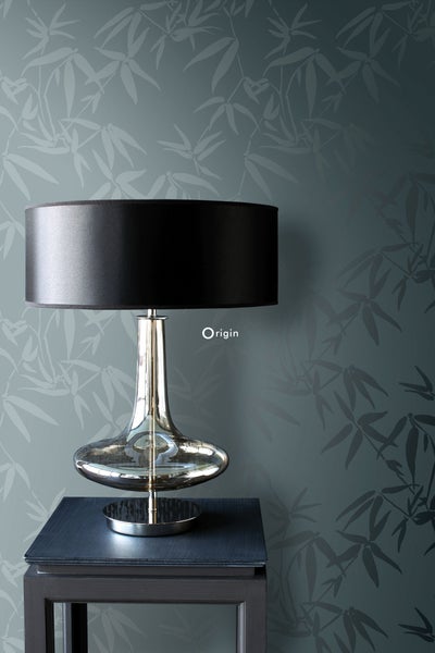 Dekorative Tischleuchte auf einem Tisch vor einer Tapete mit Bambusmuster.