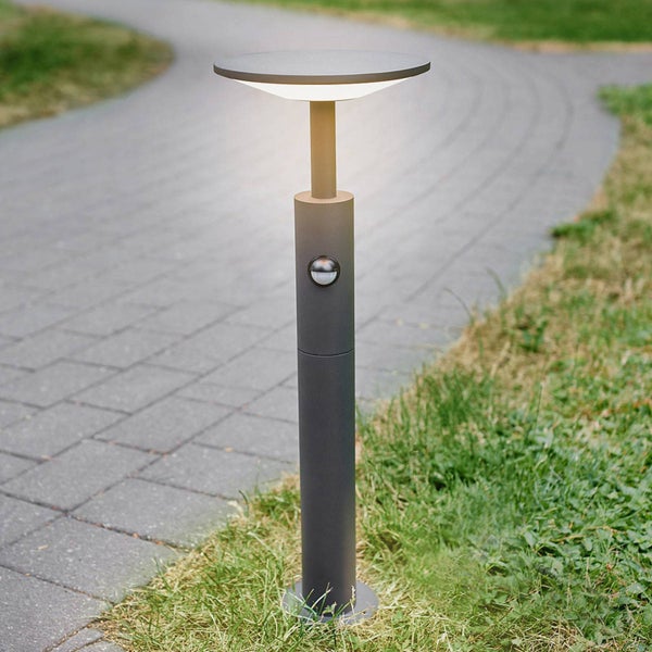 Beleuchtete moderne LED-Wegeleuchte mit Bewegungsmelder an einem gepflasterten Gartenweg neben einer Rasenfläche.