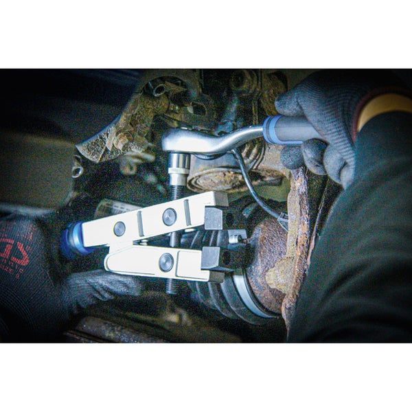 Eine Person benutzt ein Traggelenkwerkzeug an einem Fahrzeug.