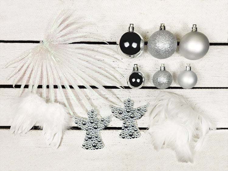 Weihnachtsbaumschmuck Set mit Kugeln in verschiedenen Größen, zwei dekorativen Engeln und künstlichen Federn auf einem Untergrund aus Holzlatten.