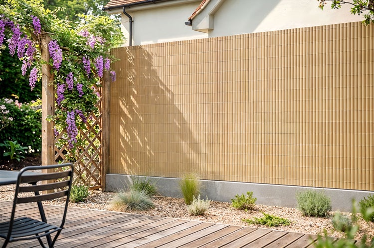 Sichtschutzmatte aus Kunststoff als Sichtschutz für den Garten an einem Holzzaun mit blühenden Kletterpflanzen und Holzterrasse.