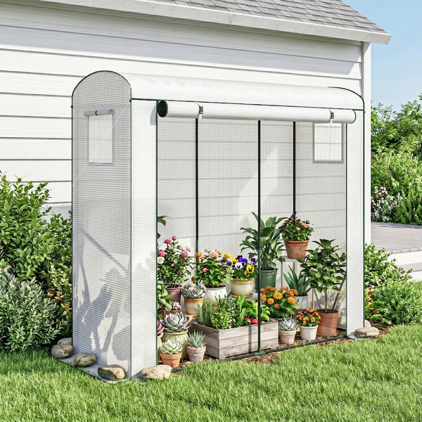 Folien-Gewächshaus mit aufrollbarer Tür im Garten neben einem Haus mit verschiedenen Topfpflanzen im Inneren.