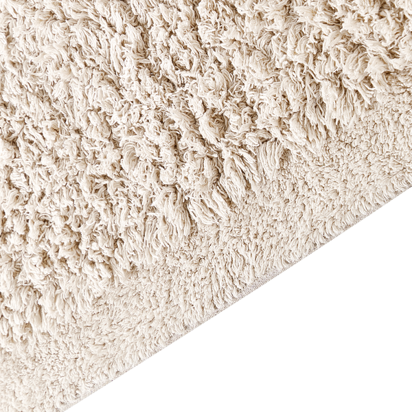 Nahaufnahme eines cremefarbenen Hochflor-Badeteppichs mit weicher, zotteliger Struktur.