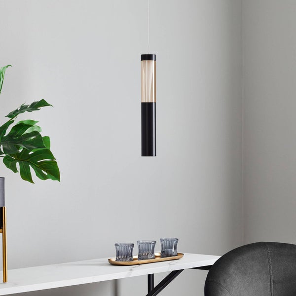 Zylinderförmige Pendelleuchte in Schwarz und Gold-Optik über einem weißen Tisch mit Marmormuster. Helle, moderne Raumatmosphäre.