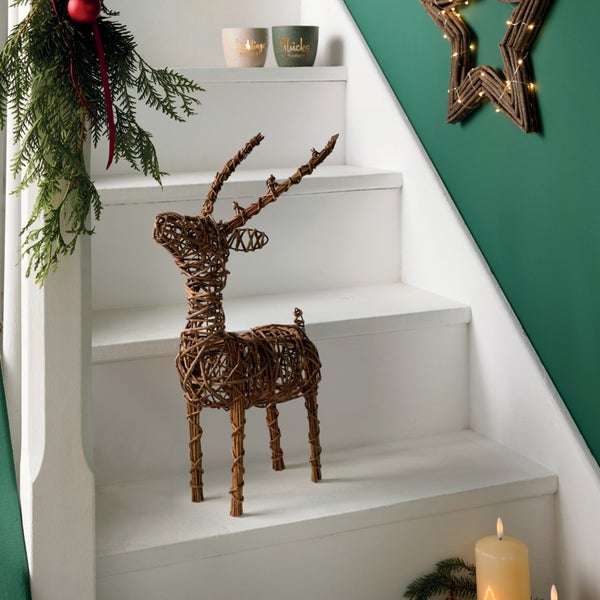 Deko Rentier aus Weidengeflecht auf einer weißen Treppe dekoriert mit weihnachtlichen Elementen und Lichterkette an der Wand.