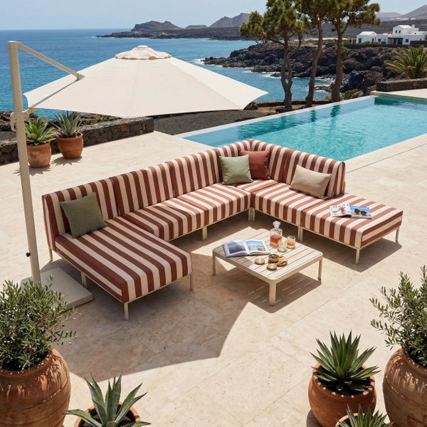 Gestreifte Garten-Lounge mit Ecksofa, Tisch und Ampelschirm auf einer hellen Terrasse am Pool mit Meerblick und Pflanzen in Terrakotta-Töpfen.