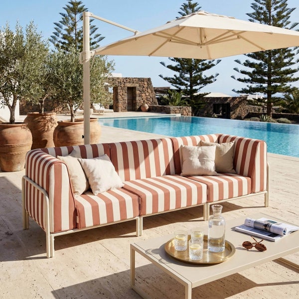 Gestreiftes dreisitziges Outdoor-Lounge-Sofa mit Couchtisch und Ampelschirm auf einer Steinterrasse am Pool.